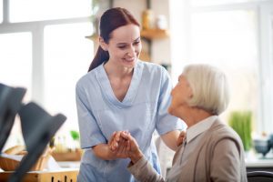 Red-haired caregiver smiling and talking to aged woman