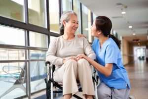 friendly staff caregiver of nursing home talking to asian senior woman in hallway