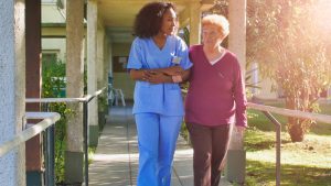 African female doctor talking to elderly retired woman in the hospital yard. Happiness and retirement concept.
