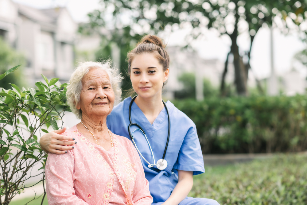 Nurse caregiver embracing happy Asian elderly woman outdoor in the park. Focused on eldery woman