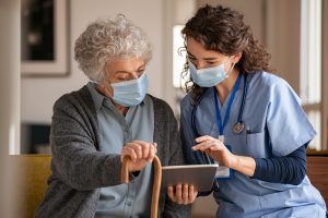 Old woman with nurse with surgical mask and using digital tablet during coronavirus pandemic