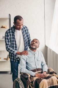 adult african american son looking at disabled senior father in wheelchair - Care Partners