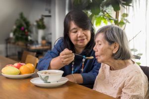 Daughter feeding elderly mother with soup - Care Partners
